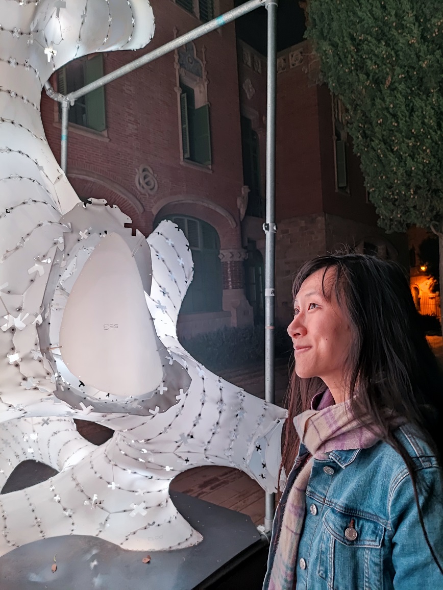 A picture of Zi beside a light installation. She has long hair and is smiling.